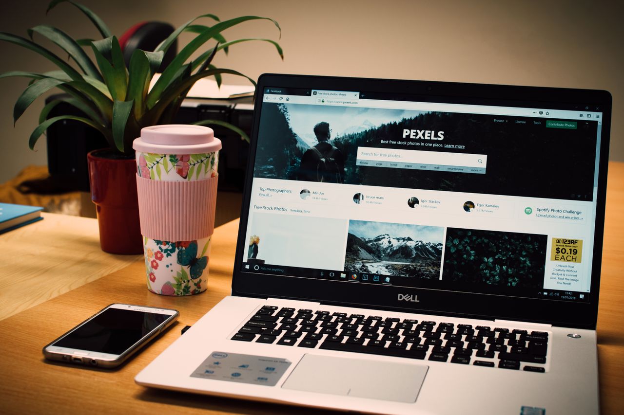 who-we-are A tidy desk setting with a laptop showing a stock photo website and a smartphone.